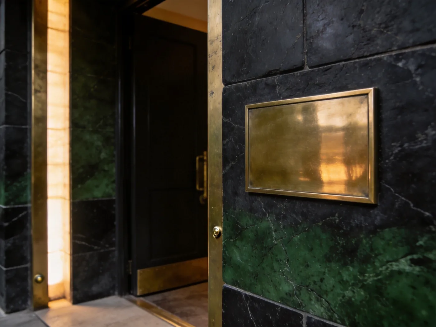 A blank polished brass plate set flush into dark stone beside a door